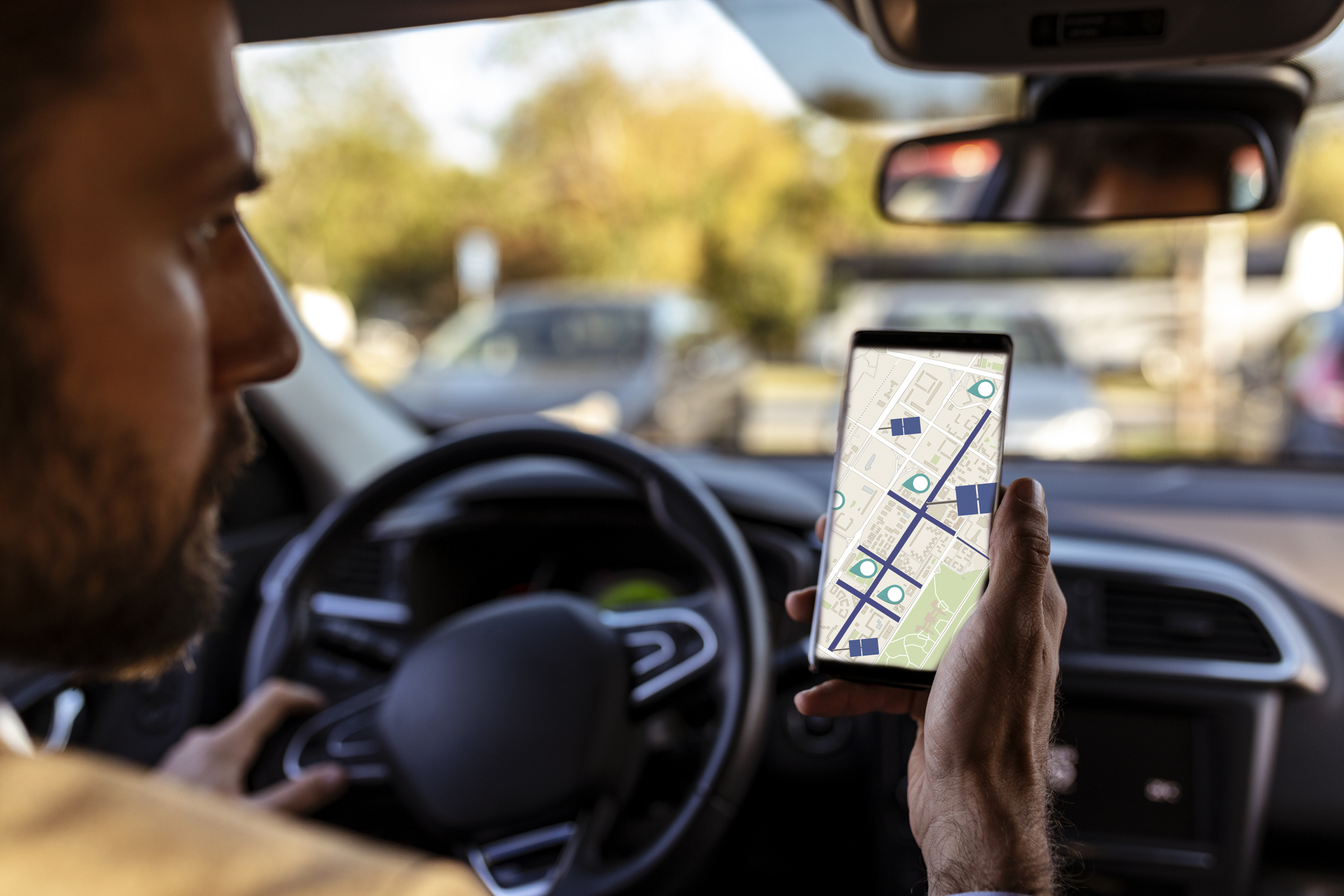 Man in a parked car holding a phone showing a map with location pins