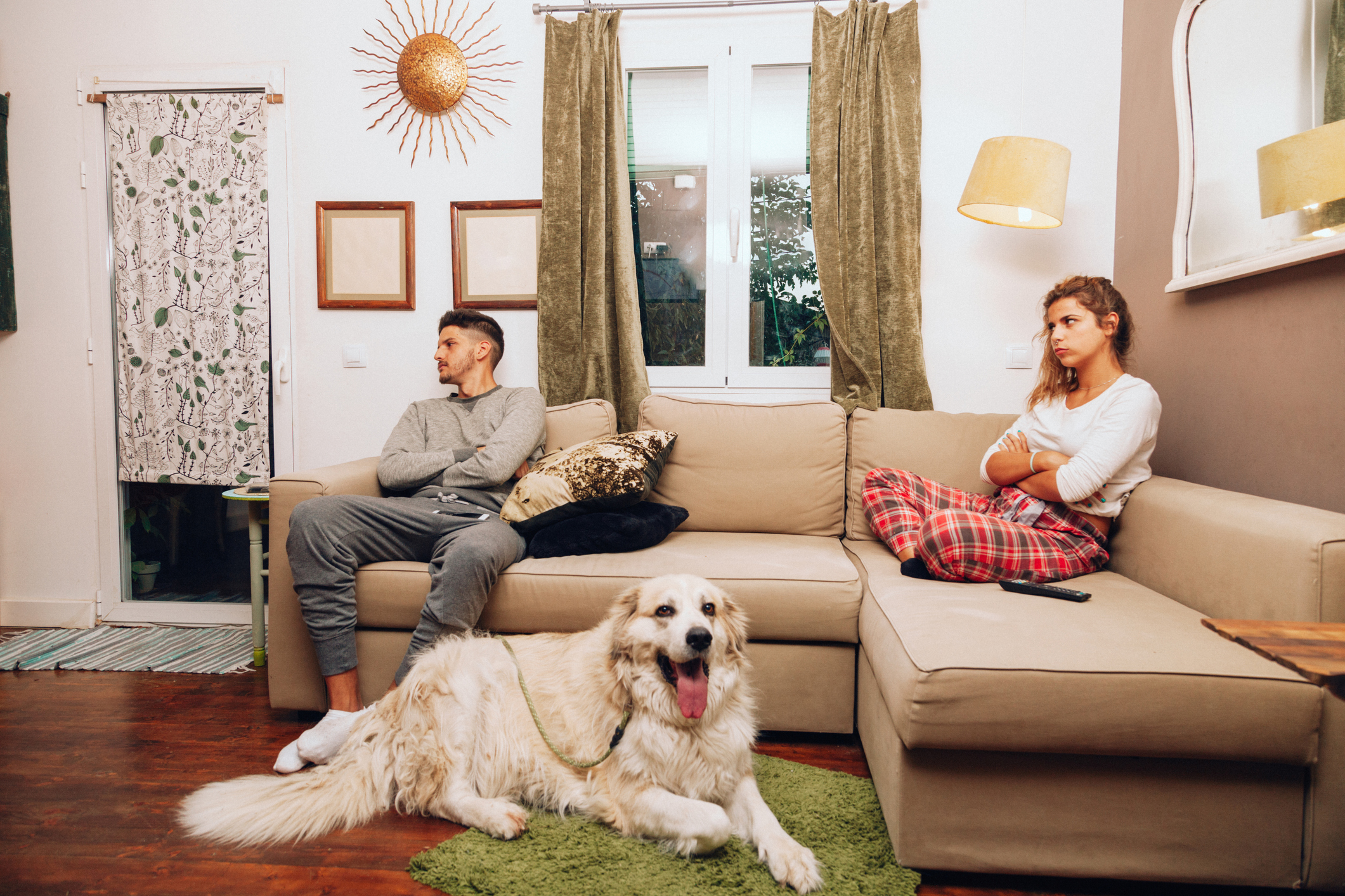 Couple sitting apart on a sofa with their dog lying on the rug between them